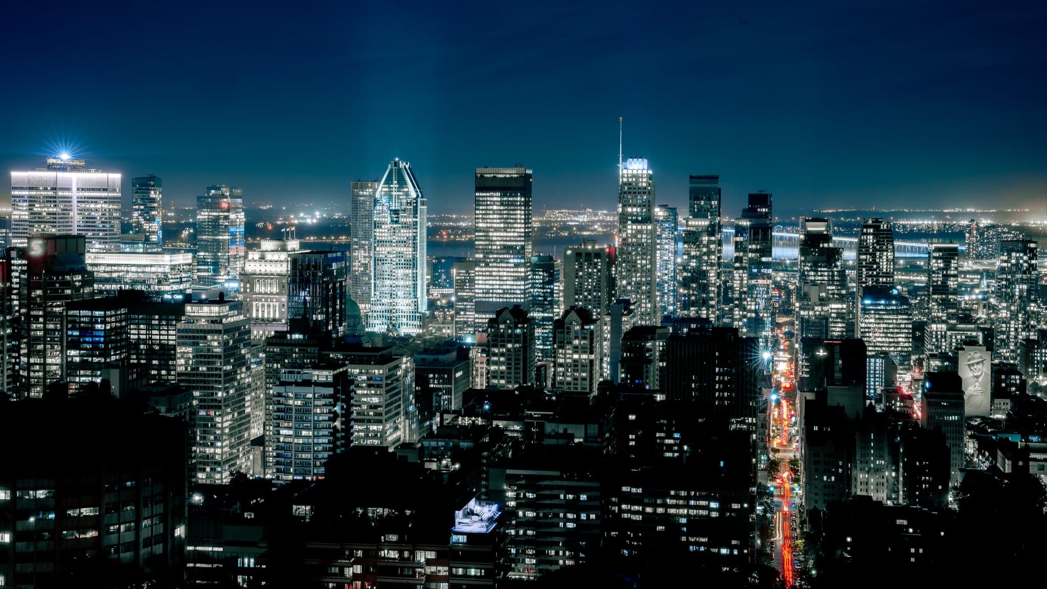 A sea of skyscrapers glimmers under the deep blue night, with veins of light weaving through the bustling metropolis.