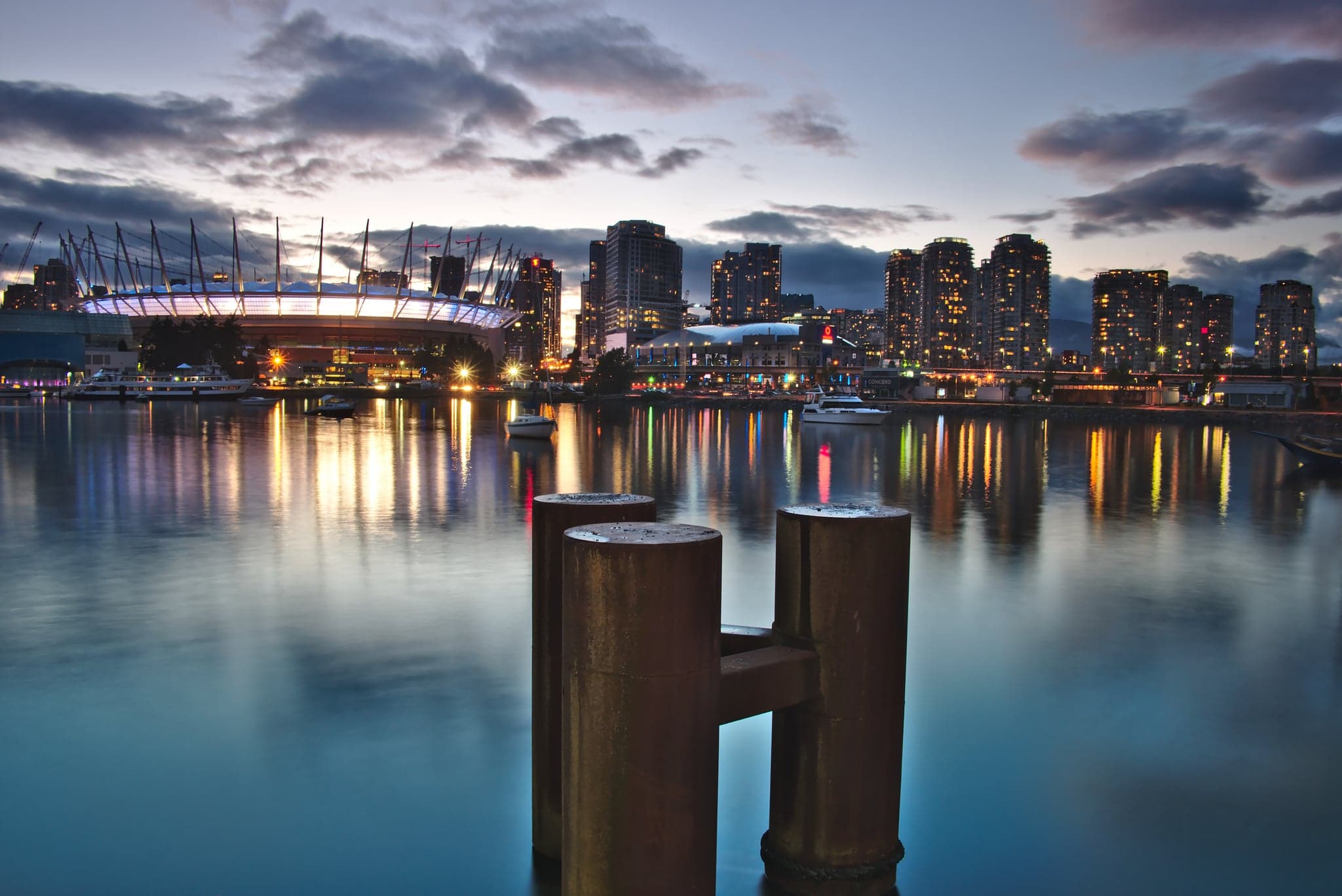 City lights shimmer across the tranquil harbor, while a dusky sky embraces the skyline in a serene twilight glow.