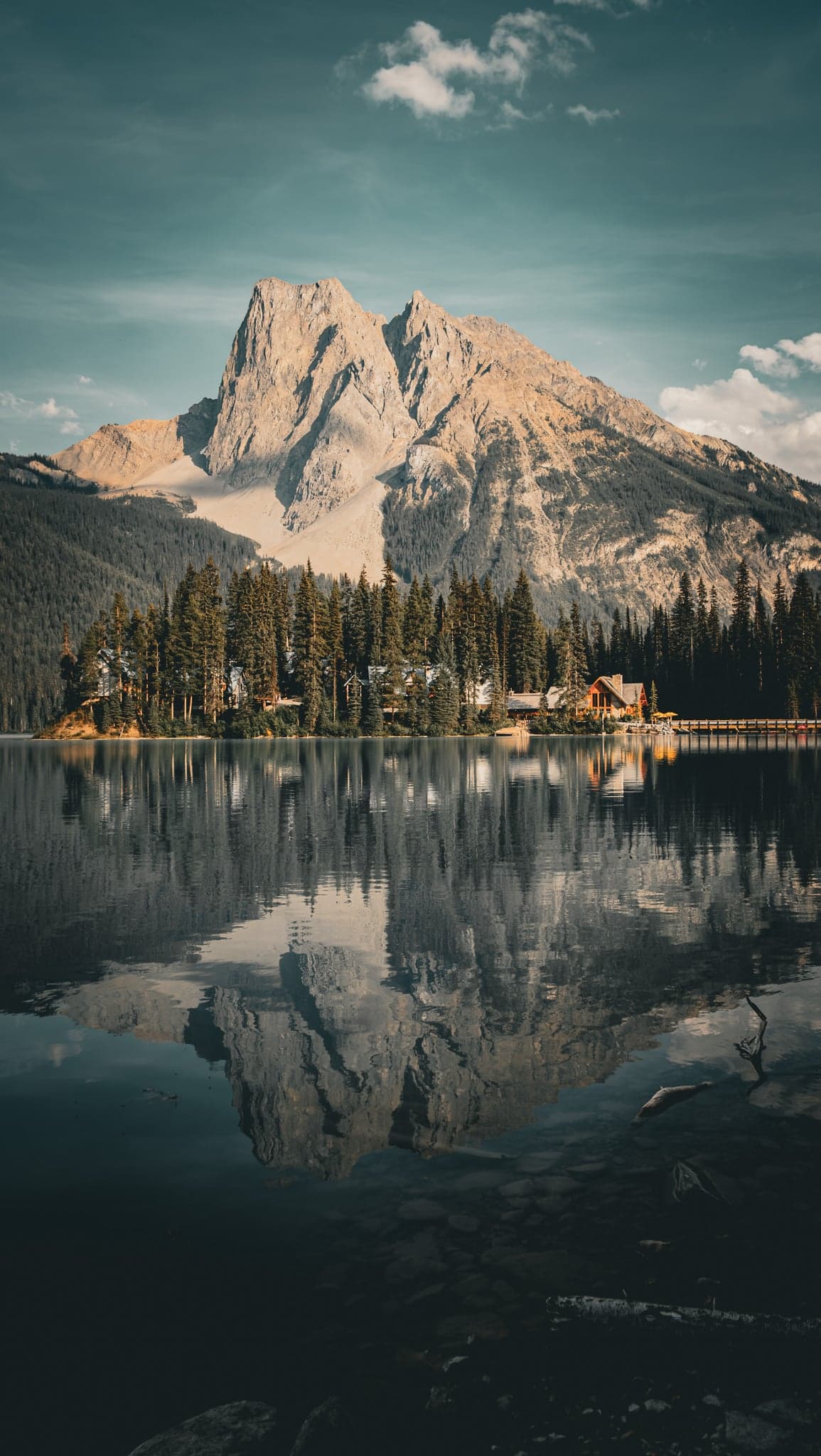 A majestic peak towers over a serene lake, its reflection mirrored perfectly in the still water beneath a tranquil sky.