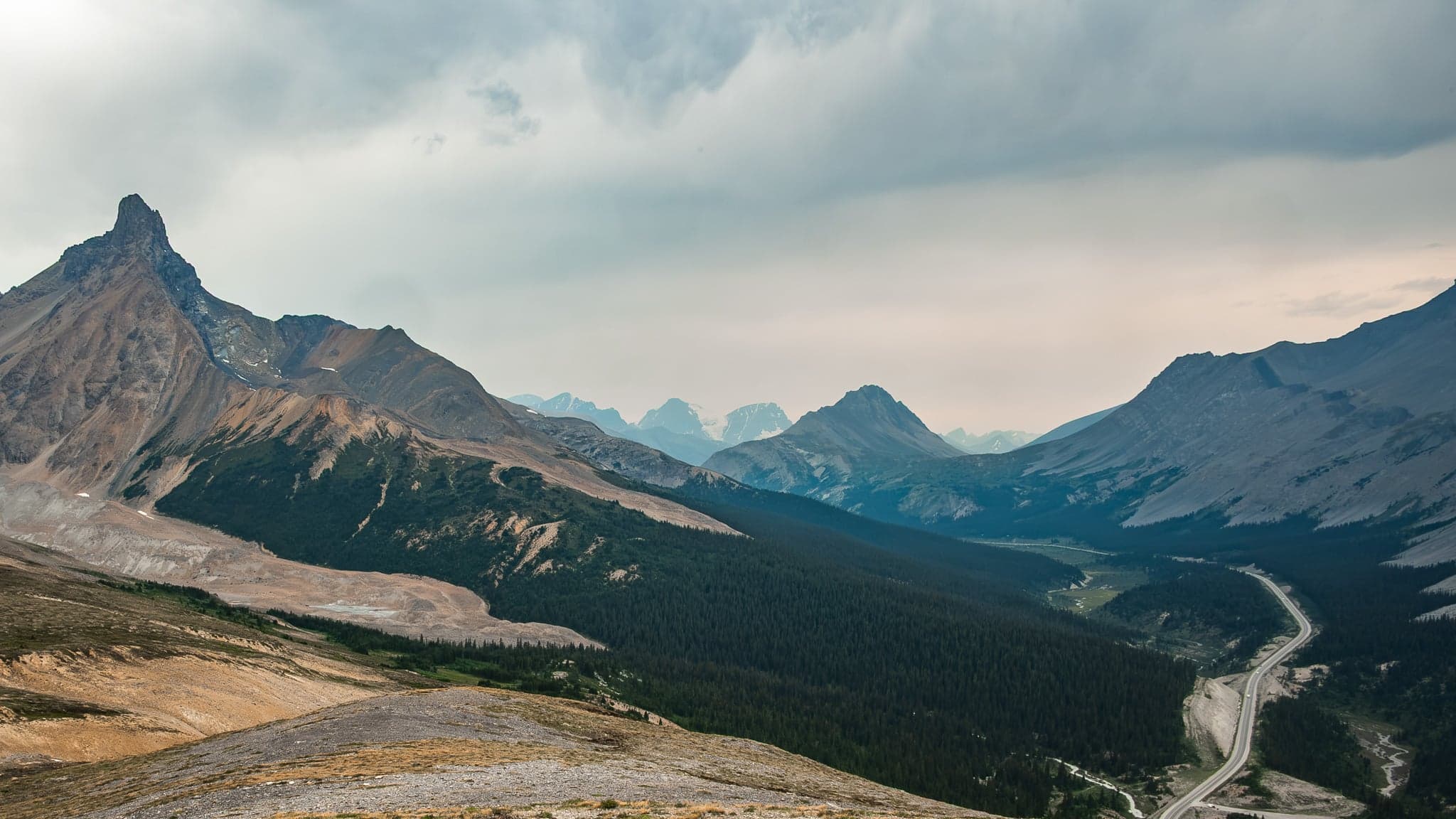 A winding road snakes through a rugged mountain pass under a brooding sky, evoking a sense of solitude and adventure.