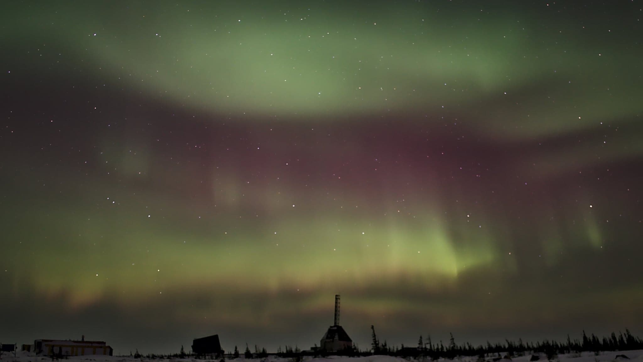 Vivid auroras dance across the night sky, casting a mystical glow over the silhouetted landscape below.