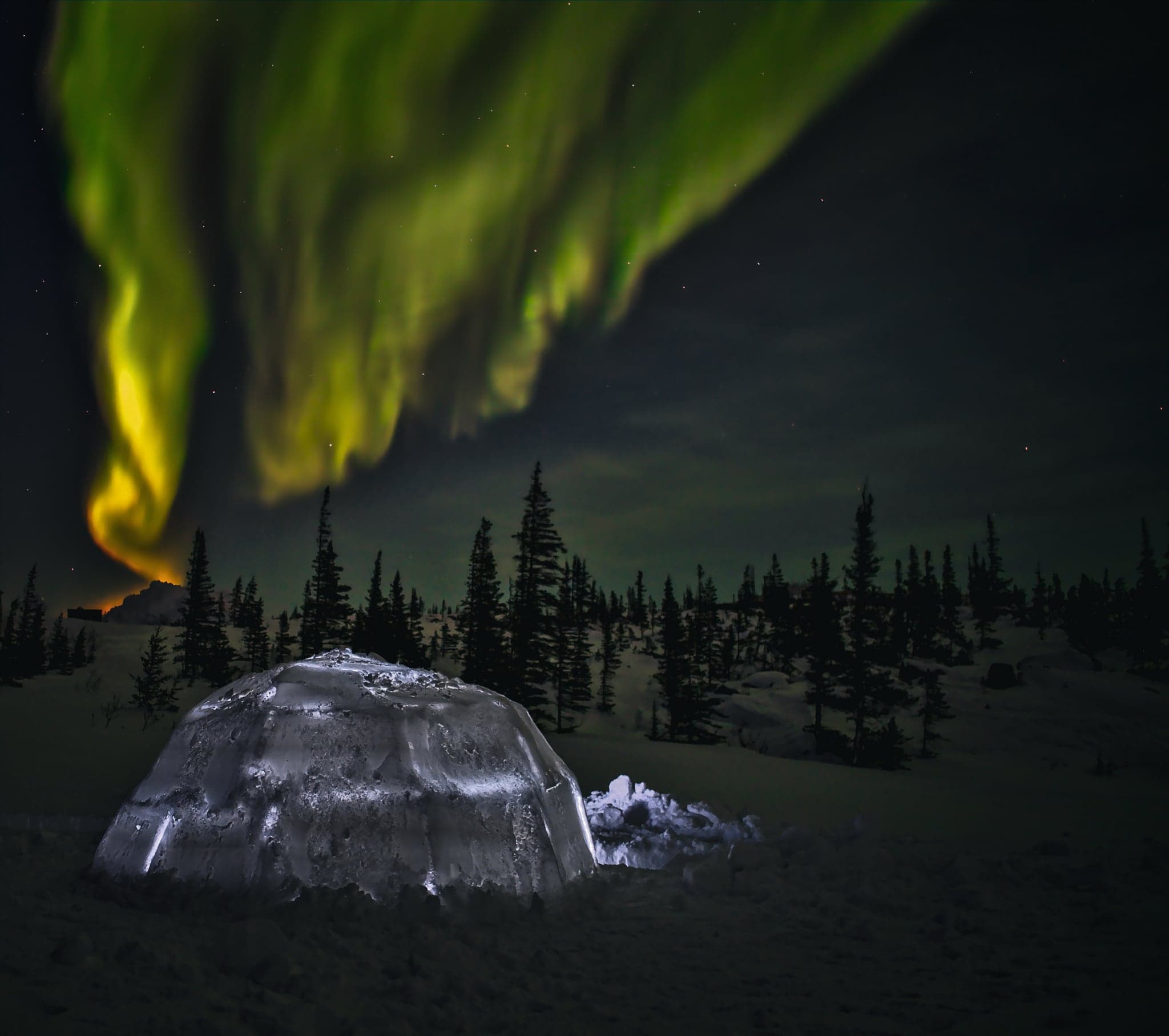 An ethereal aurora dances above a solitary igloo, casting a mystical glow over the snow-laden landscape below.