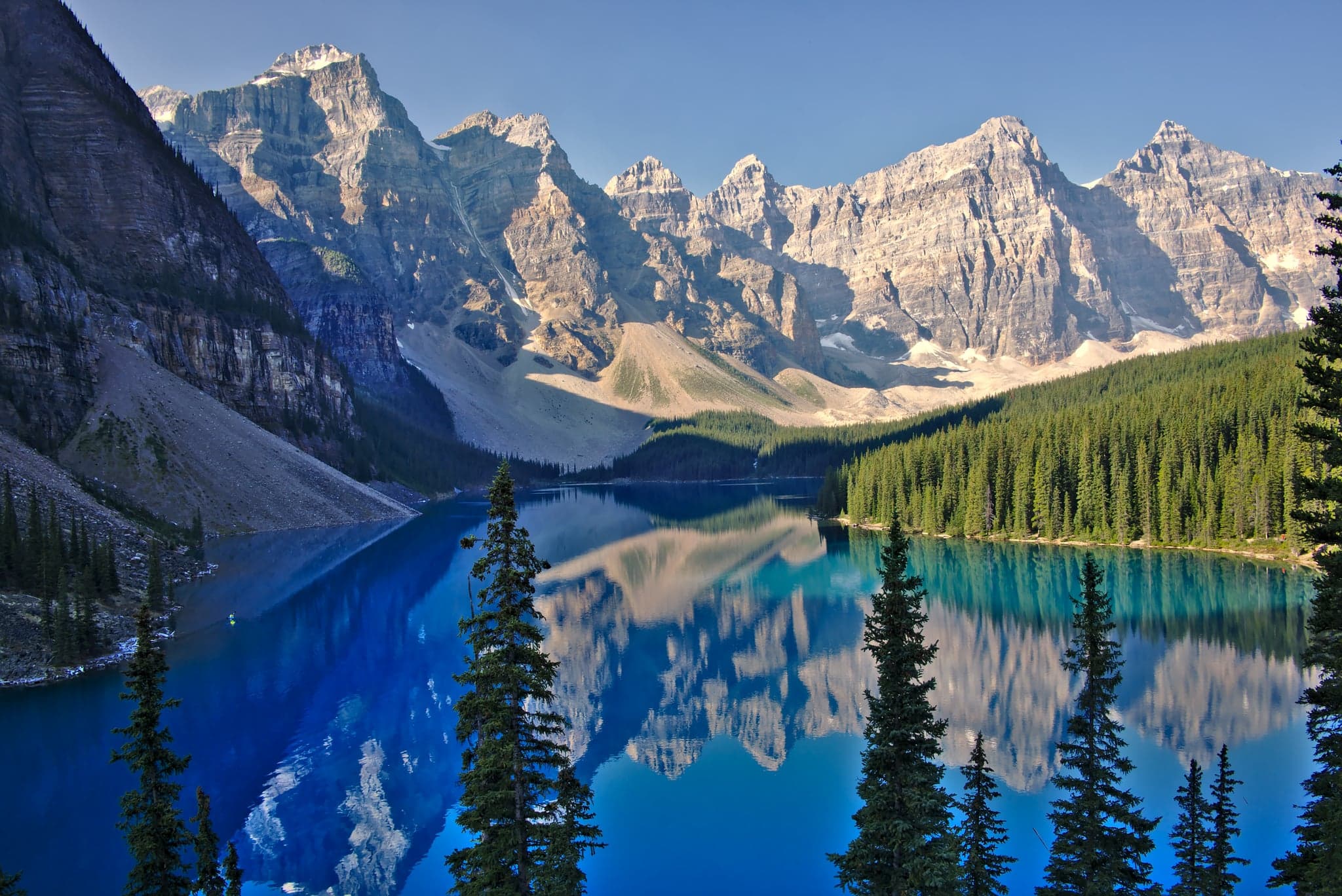 Crystal-clear lake mirrors towering peaks, their rugged grandeur softened by the deep azure sky and lush evergreen embrace.