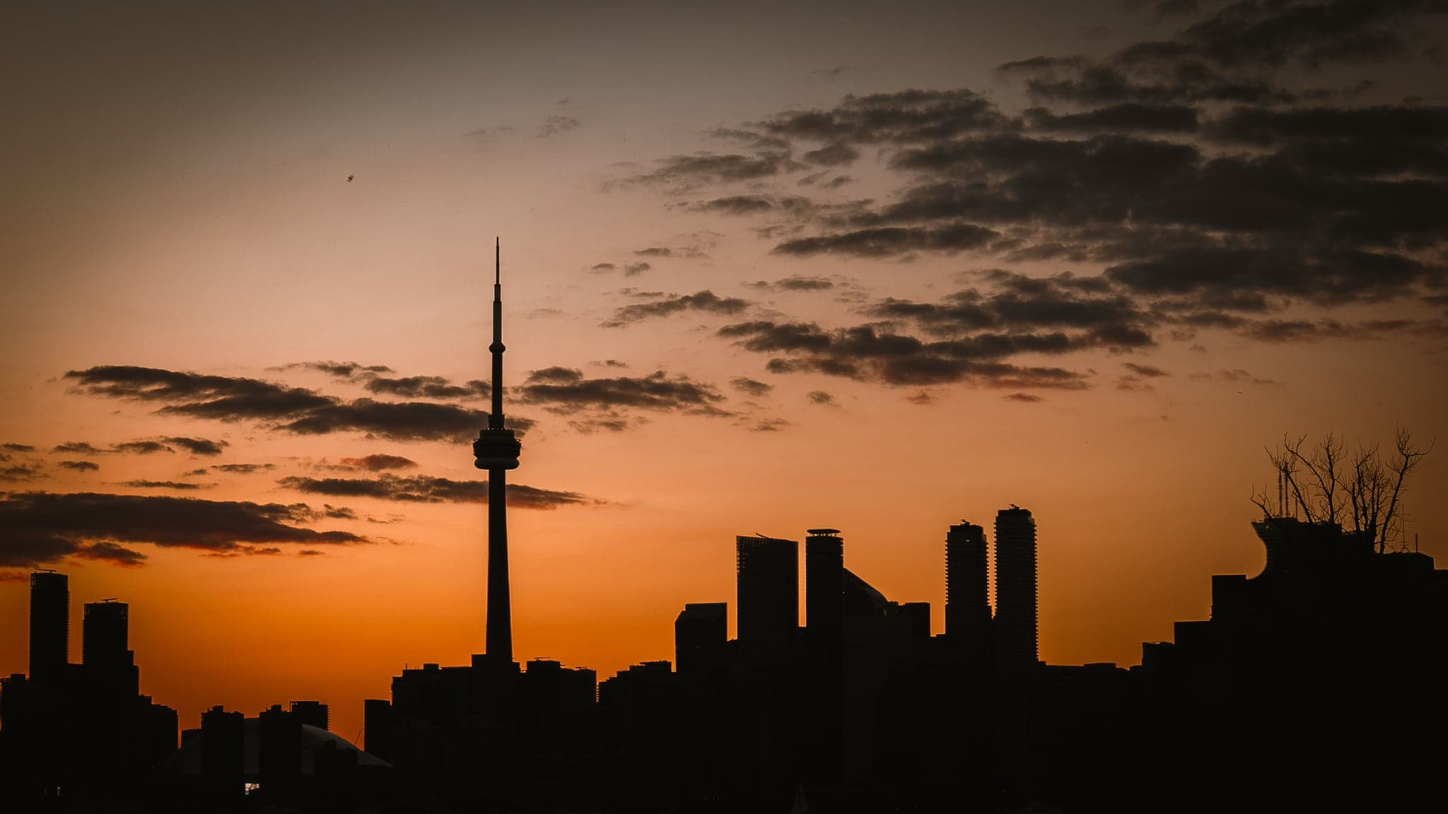The city skyline stands in stark silhouette against a fiery sunset, with the iconic tower piercing the vivid, cloud-streaked sky.